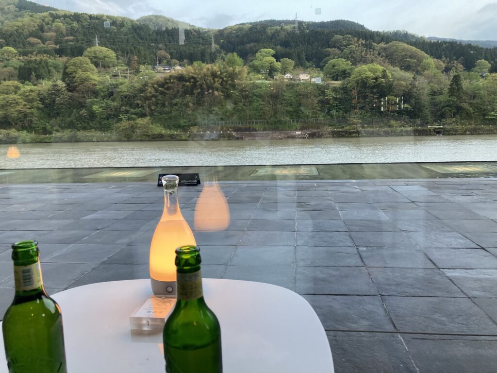 リバーリトリート雅樂倶のロビーラウンジで神通川を背景に無料のビールを飲む 